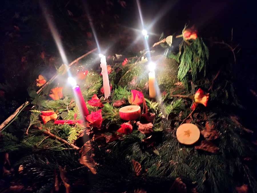 Brennende Kerzen im Dunkeln mit Apfelhälften und Blumen.